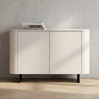 A modern sideboard cabinet with two doors, featuring a curved outer frame, a light beige finish, and black legs, set against a textured gray wall and light wood herringbone floor.