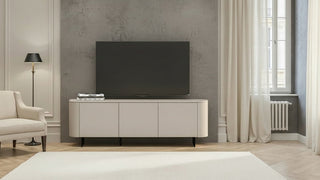 A modern beige media console with a black flat-screen TV on top, set against a textured gray wall in a styled living room with a white armchair, floor lamp, and curtains.