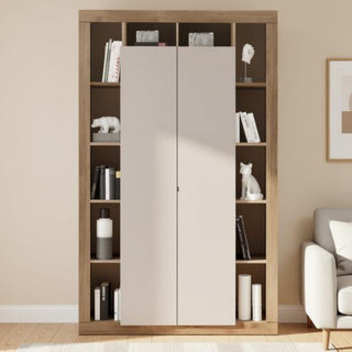 A tall built-in wardrobe or bookcase with two large light beige doors in the center and open shelving on both sides, shown in a styled room with books, decor, a rug, and part of a sofa.
