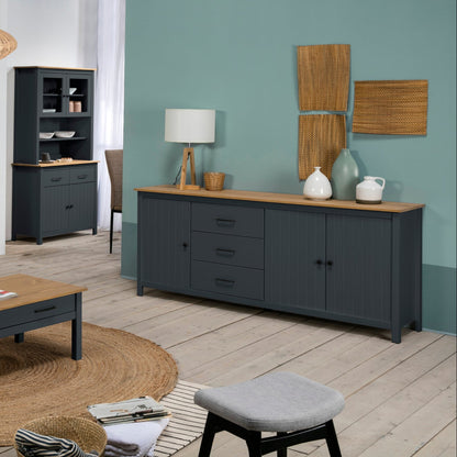 A staged living room furniture set featuring a dark gray sideboard with a light wood top, a matching TV stand, a coffee table, and a tall shelving unit, set against a teal wall and light wood floors.