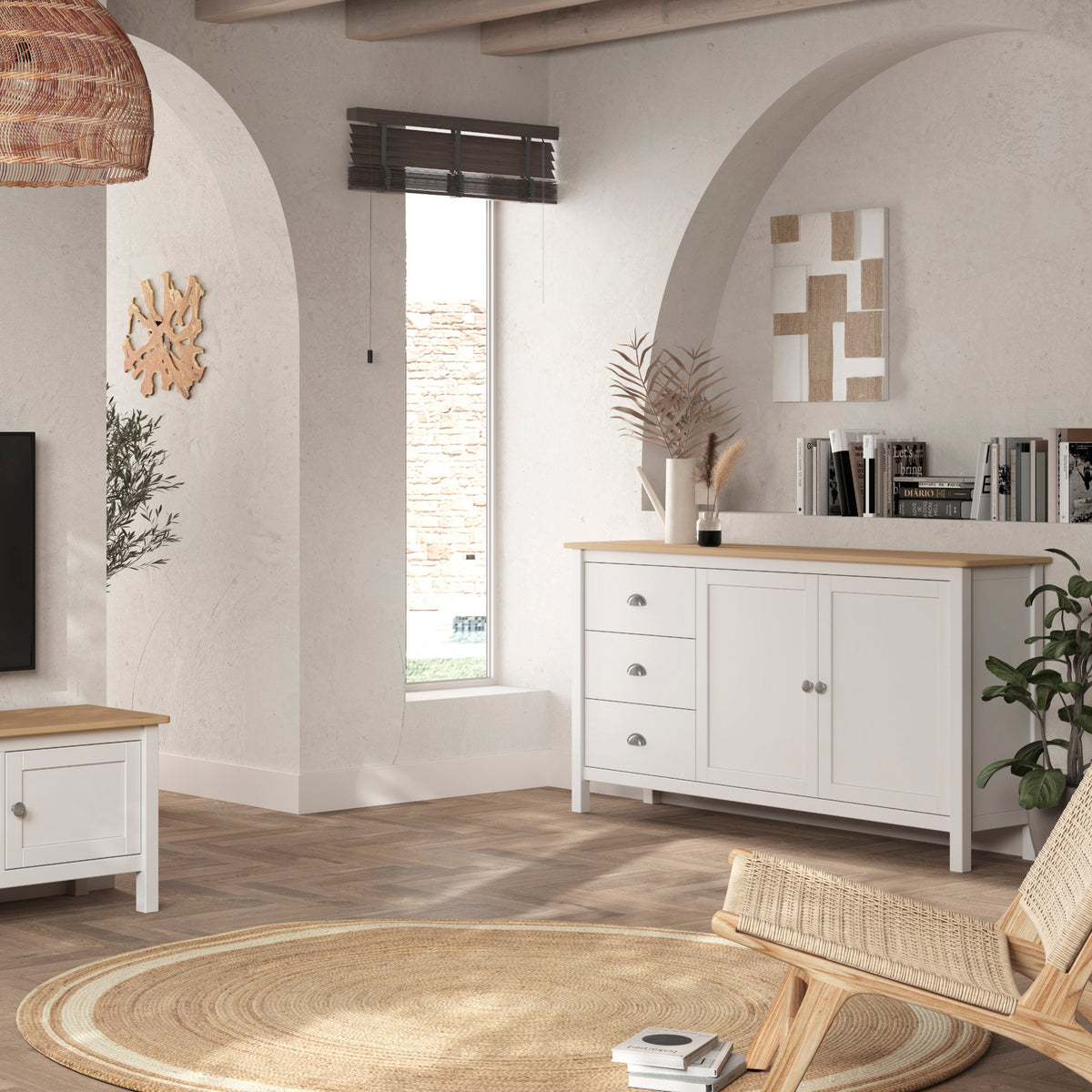 A styled living room featuring a white wooden TV stand with a light wood top, a matching white sideboard cabinet, and a woven rattan pendant light hanging above.