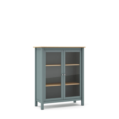 A tall, narrow storage cabinet with a muted blue-gray painted frame, a natural light wood top and shelves, and two glass doors with small round silver knobs, shown on a plain white background.