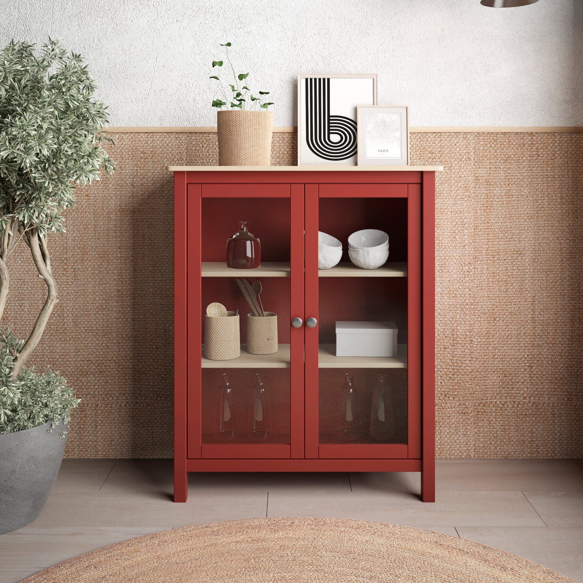 A red wooden cabinet with glass doors and light wood shelves stands against a textured wall in a styled interior. The cabinet is decorated with small home decor items, framed art, and a potted plant, with two pendant lights and a woven rug visible in the room.
