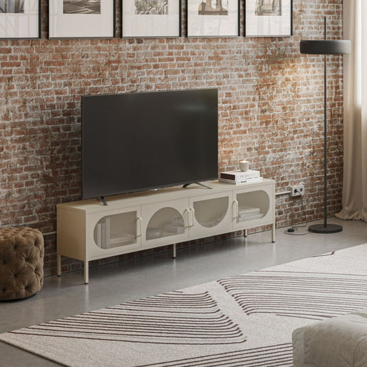 A modern living room featuring a white TV stand with arched glass-front doors, a black flat-screen TV, a black floor lamp, a brick wall with framed black-and-white prints, and a large window with sheer curtains.