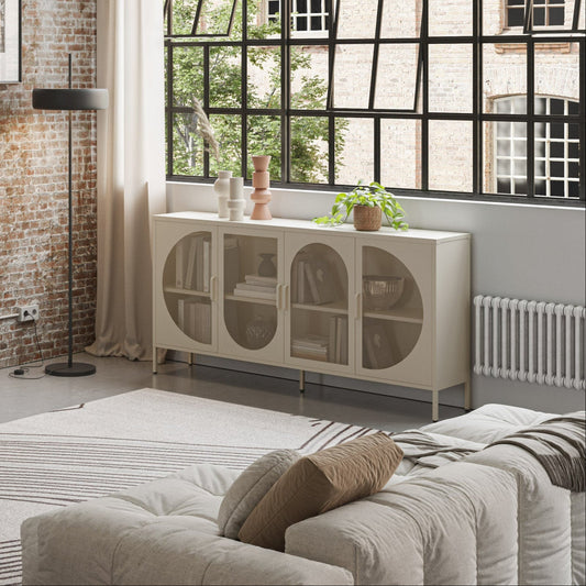 A modern living room featuring a cream sideboard cabinet with arched glass doors, styled in a bright room with a brick wall, large black-framed window, and a light-colored sofa.