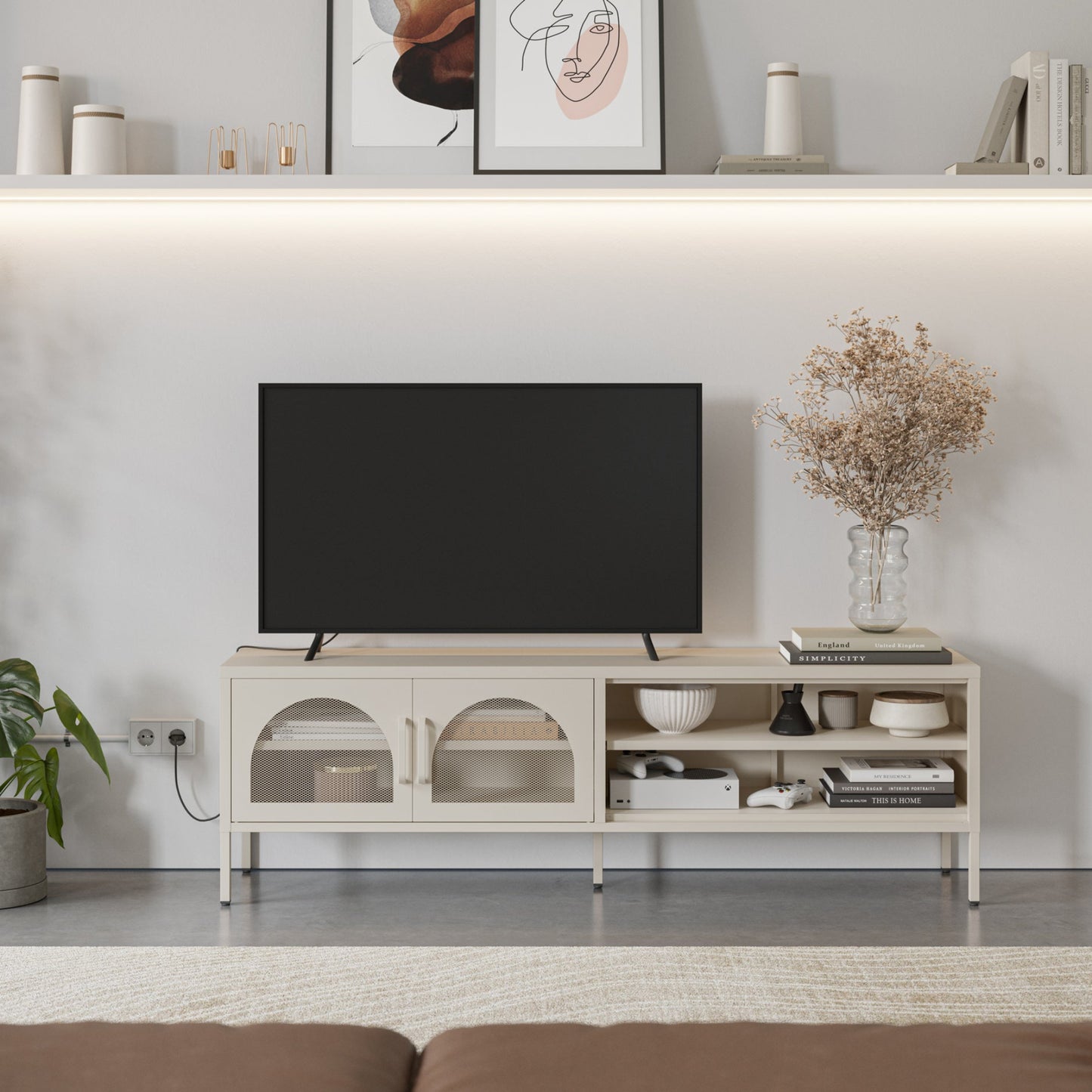 A modern light beige TV stand console with open shelves and arched cabinet doors, styled in a living room setting with a black flat-screen TV, decorative books, a vase of dried flowers, and wall shelves above.