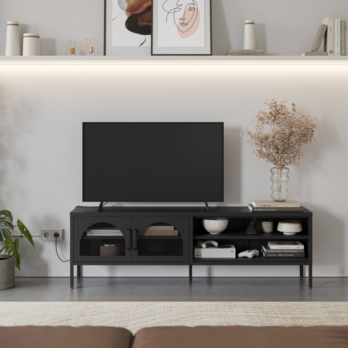 A modern black TV stand console with open shelving and two cabinet doors, styled in a minimalist living room setting with a television, decorative items, and a vase of dried flowers.