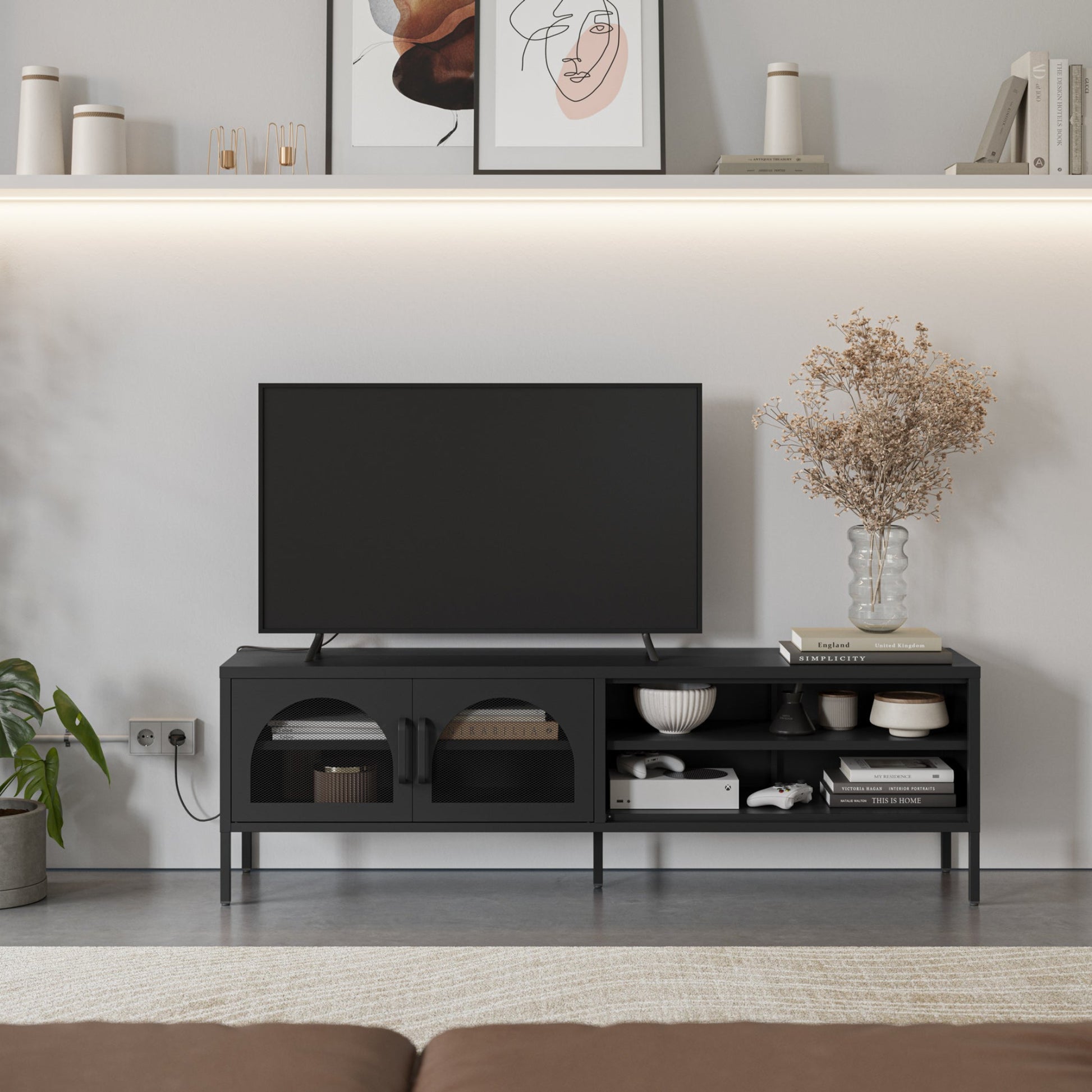 A modern black TV stand console with open shelving and two cabinet doors, styled in a minimalist living room setting with a television, decorative items, and a vase of dried flowers.