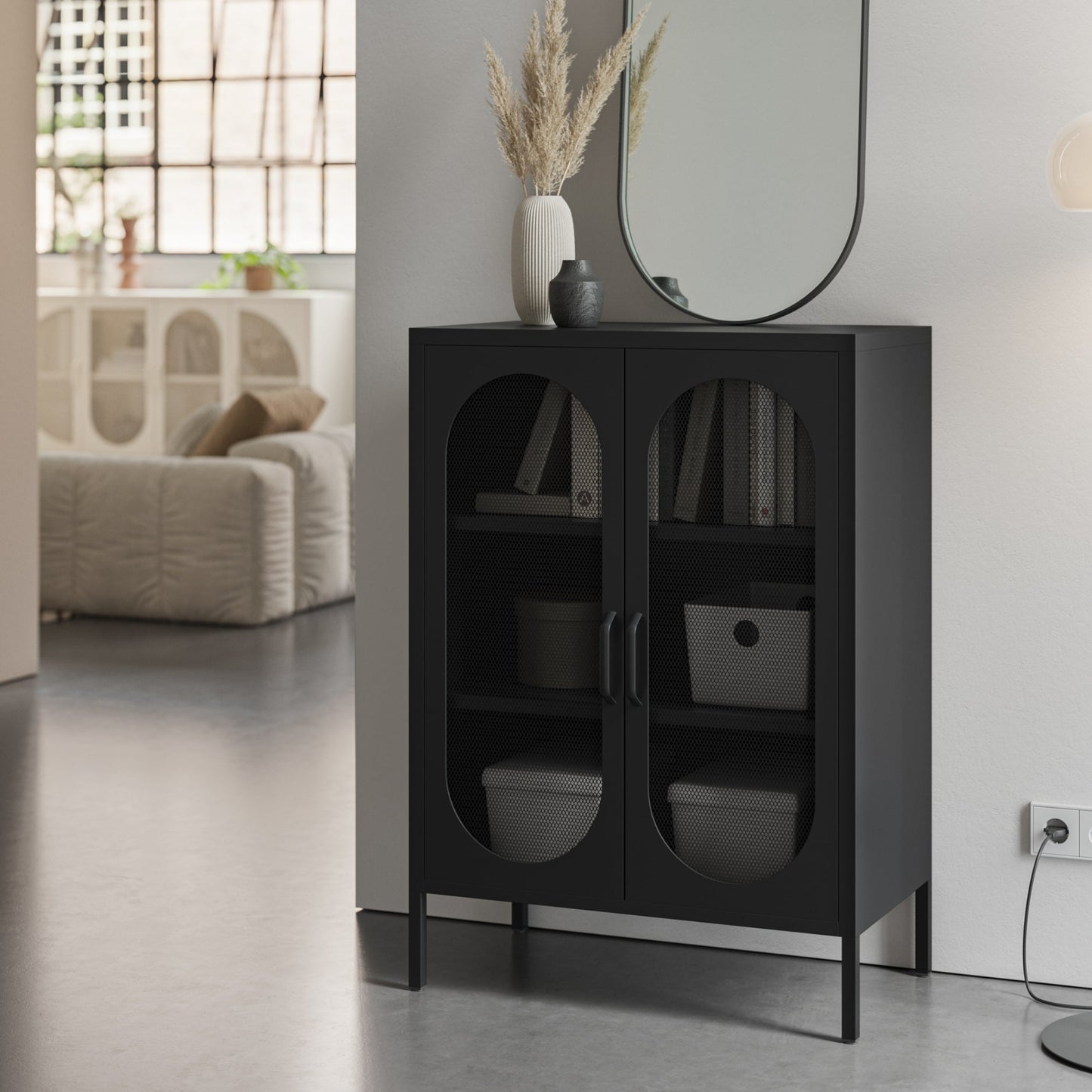 A modern black storage cabinet with two arched glass doors stands in a minimalist room setting next to a white wall, holding books and storage bins.