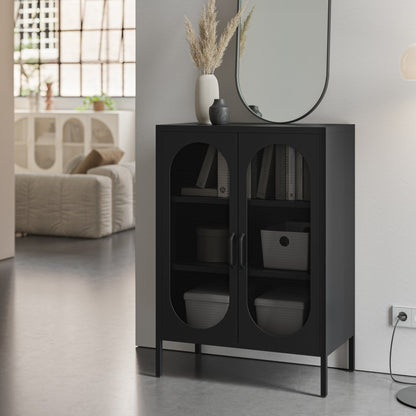 A modern black storage cabinet with two arched glass doors stands in a minimalist room setting next to a white wall, holding books and storage bins.