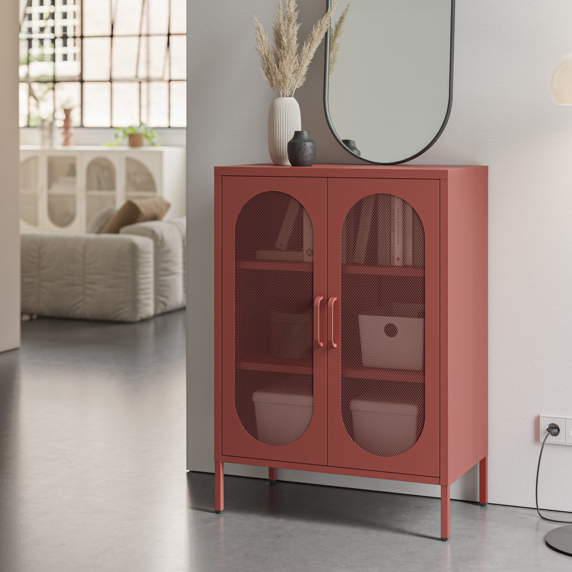 A terracotta red two-door cabinet with arched glass doors and brass handles, styled in a modern living room setting.