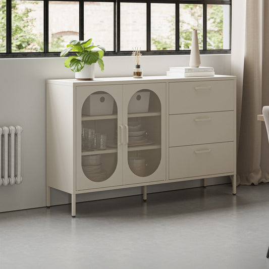 A cream-colored sideboard cabinet in a modern dining room setting, featuring two glass-front doors on the left and three drawers on the right, styled with a small plant and decorative items on top.