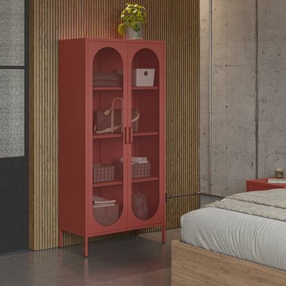 A tall coral-red two-door storage cabinet with arched glass panels stands in a bedroom setting against a slatted wood wall, with a bed and concrete wall visible.