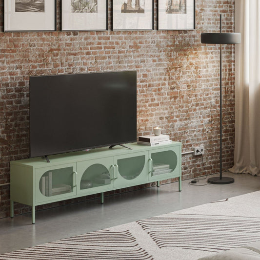 A styled living room featuring a mint green TV stand and matching sideboard cabinet against a rustic brick wall, with a black floor lamp, framed wall art, and a large window.