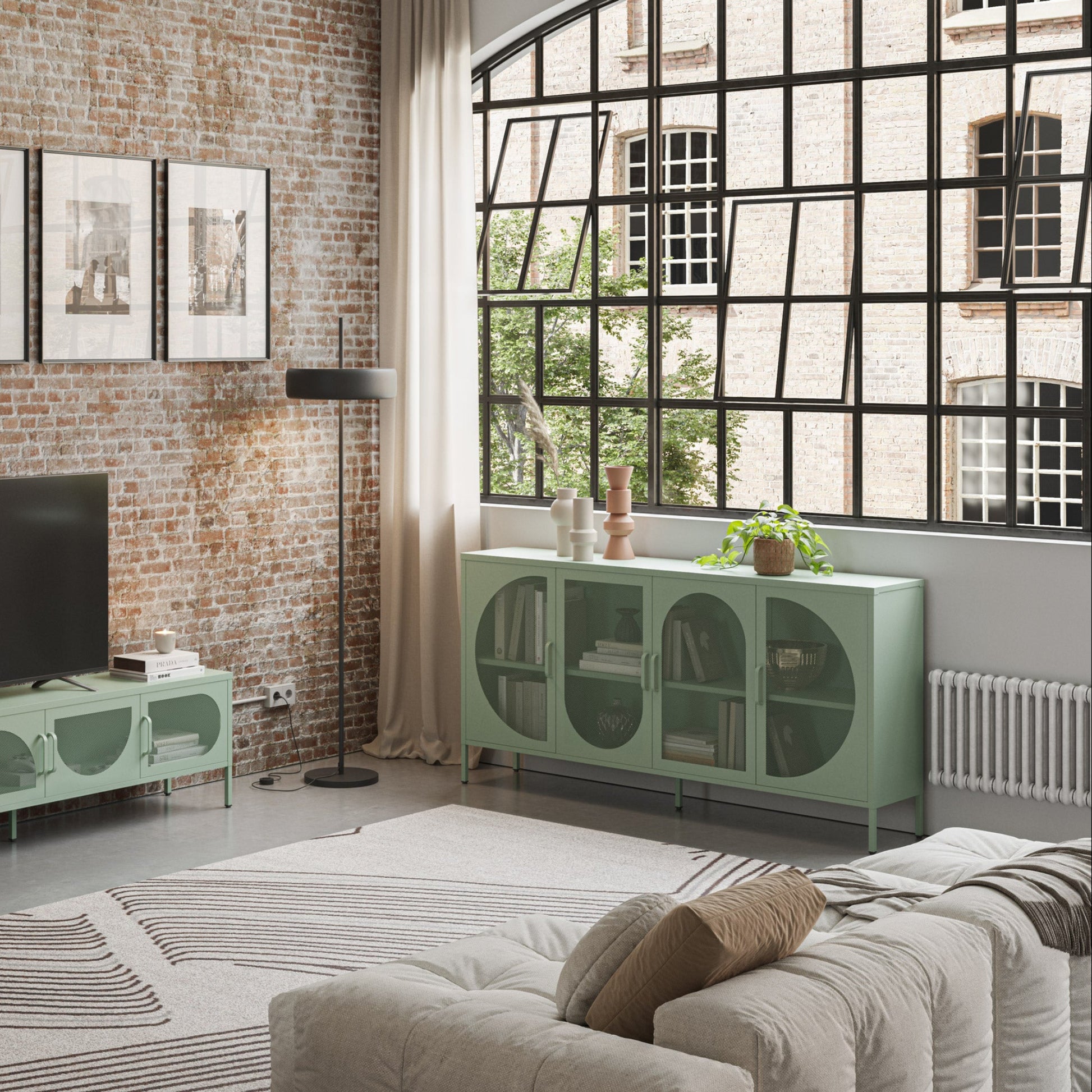 A styled living room featuring a mint green TV stand and matching sideboard cabinet against a rustic brick wall, with a black floor lamp, framed wall art, and a large window.