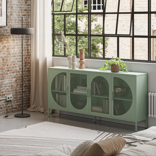 A styled living room featuring a mint green TV stand and matching sideboard cabinet against a rustic brick wall, with a black floor lamp, framed wall art, and a large window.