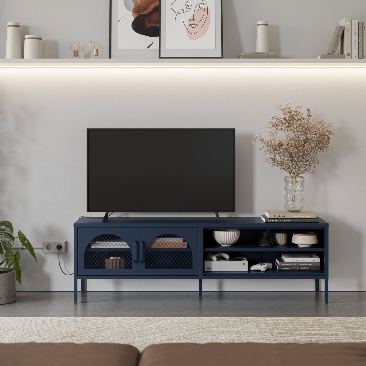 A navy blue modern TV stand with open and arched storage compartments, styled in a living room setting with a black television on top, decorative items, and a vase of dried flowers.