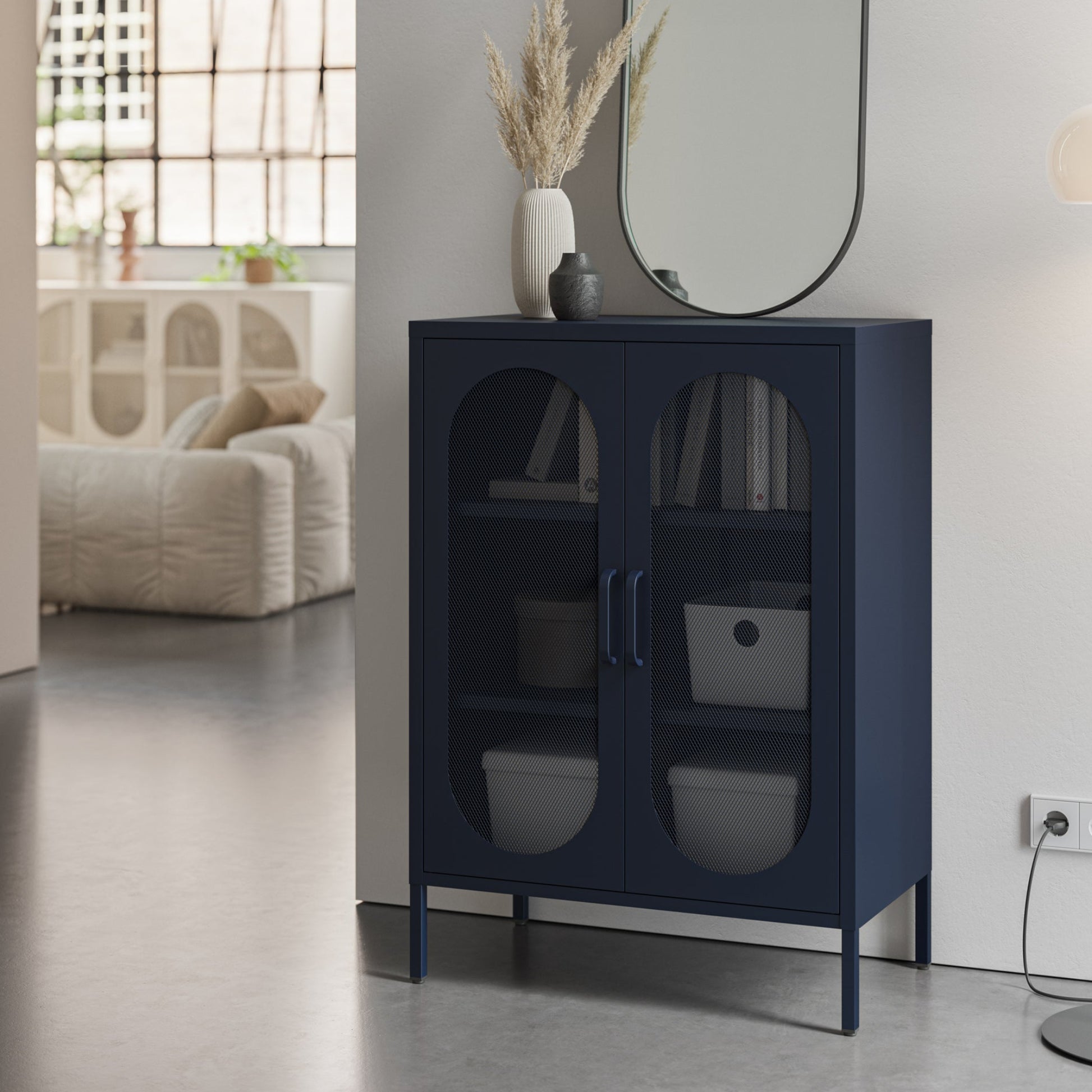 A navy blue storage cabinet with two arched glass doors stands in a modern room setting next to a white wall, holding storage bins and books.
