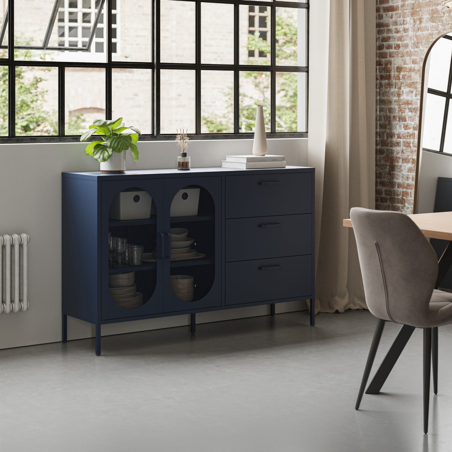 A navy blue wooden sideboard cabinet with two glass-front doors and three drawers, styled in a modern loft room next to a dining table and chair.