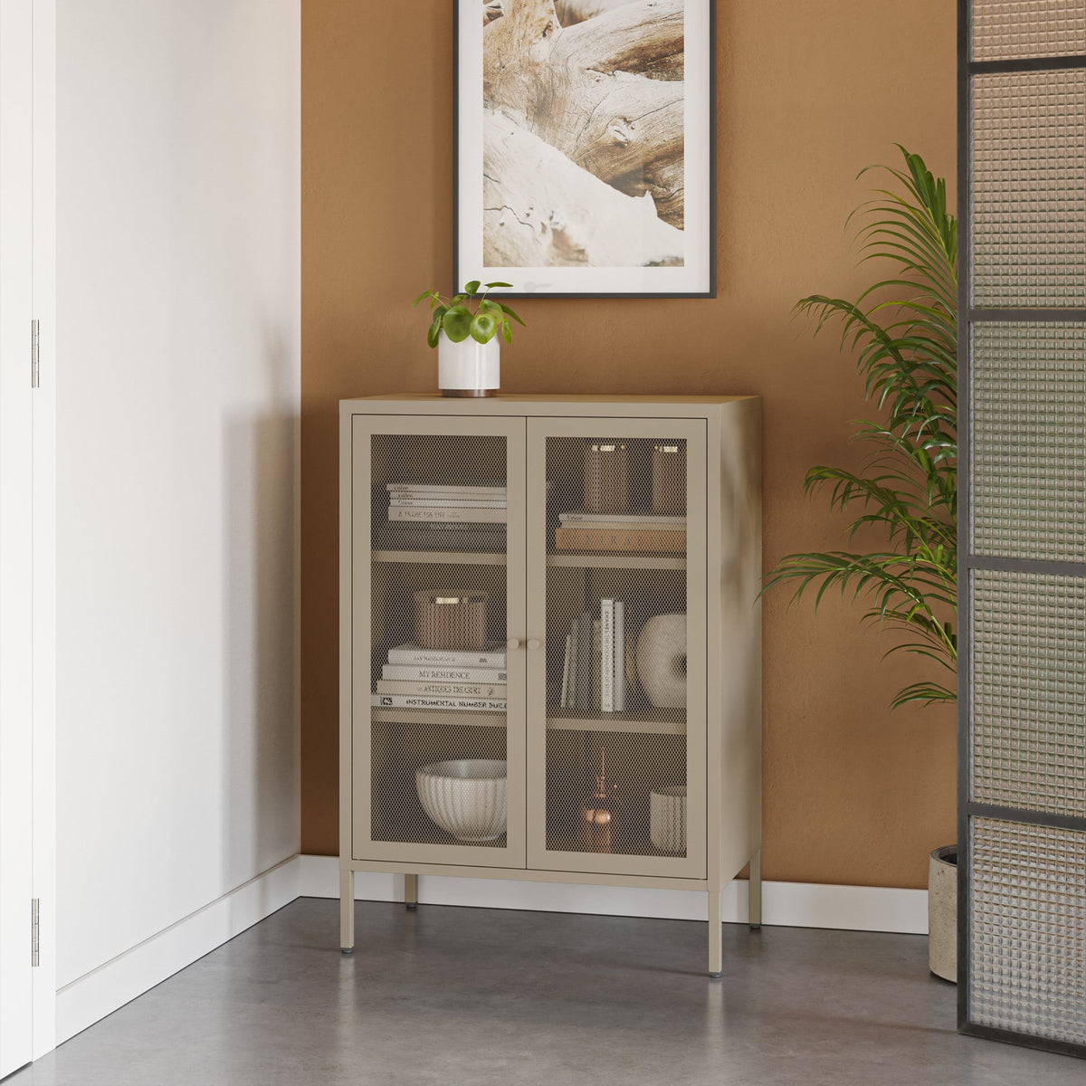 Beige cabinet with glass doors against a wall with a framed picture and plant.