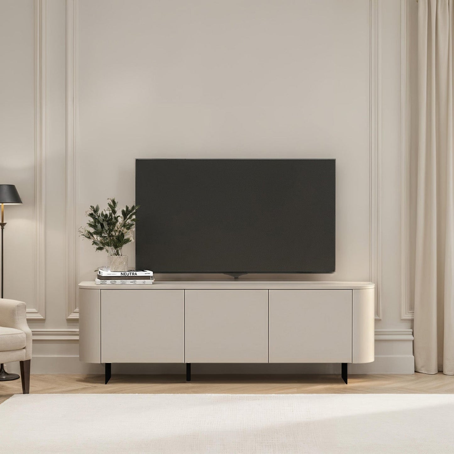 Modern living room with a television on a white cabinet, light-colored walls, and a window with curtains.