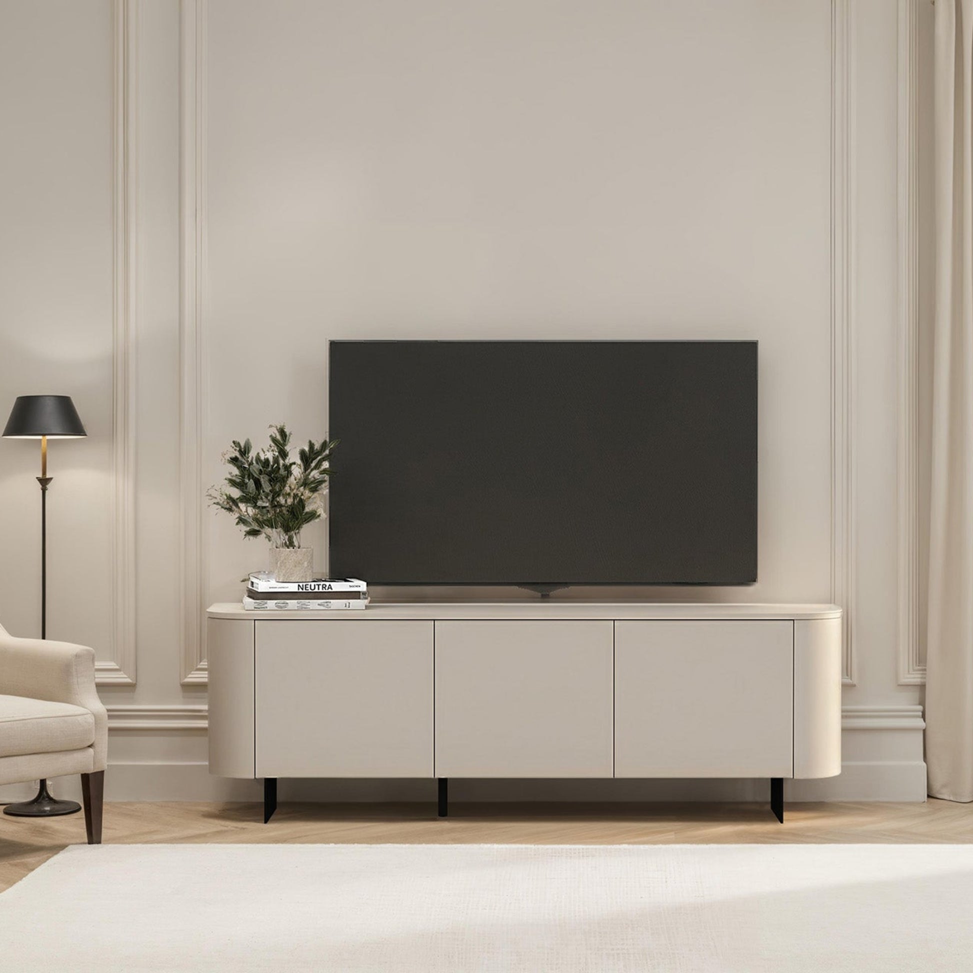 Modern living room with a television on a white cabinet, light-colored walls, and a window with curtains.