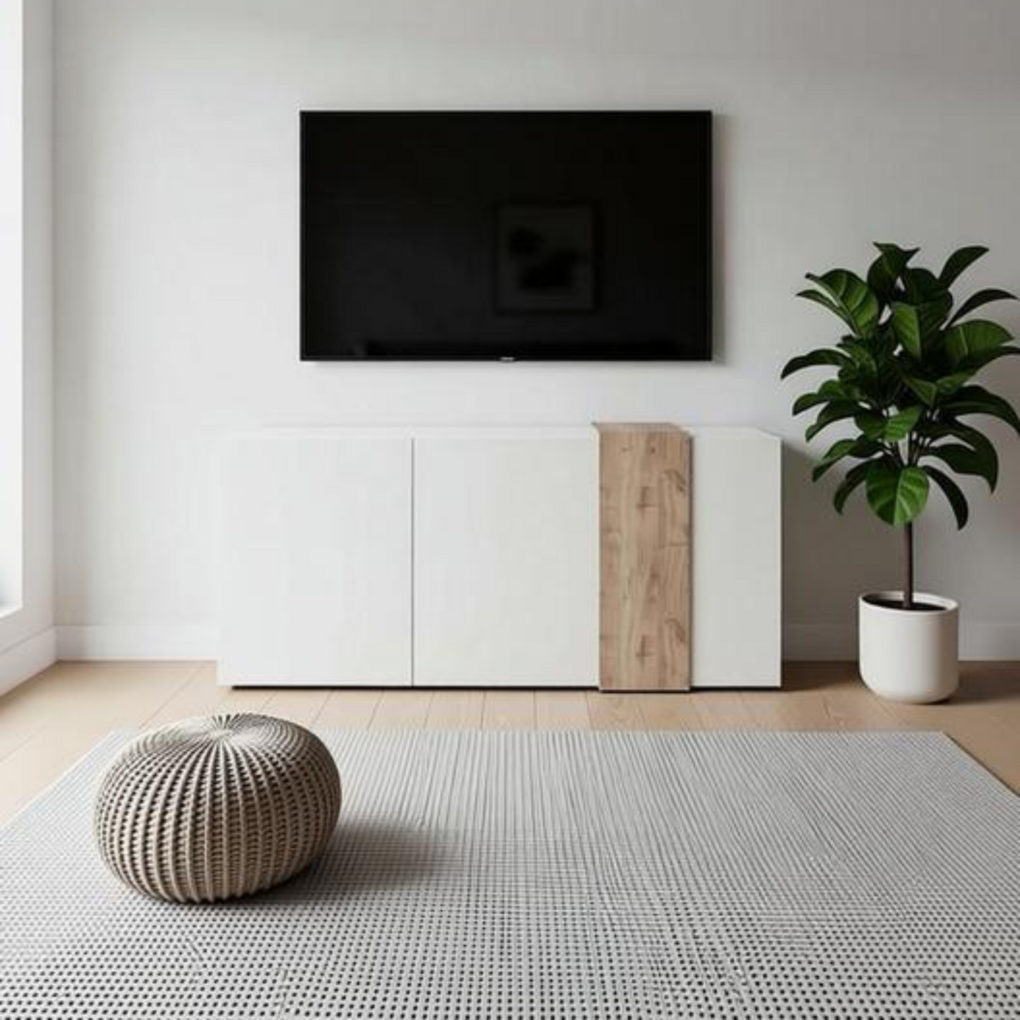 A modern living room setup featuring a black flat-screen TV mounted on a white wall above a white media console with a vertical wood accent panel. A large green potted plant stands to the right, and a round woven pouf sits on a textured gray rug in the foreground.
