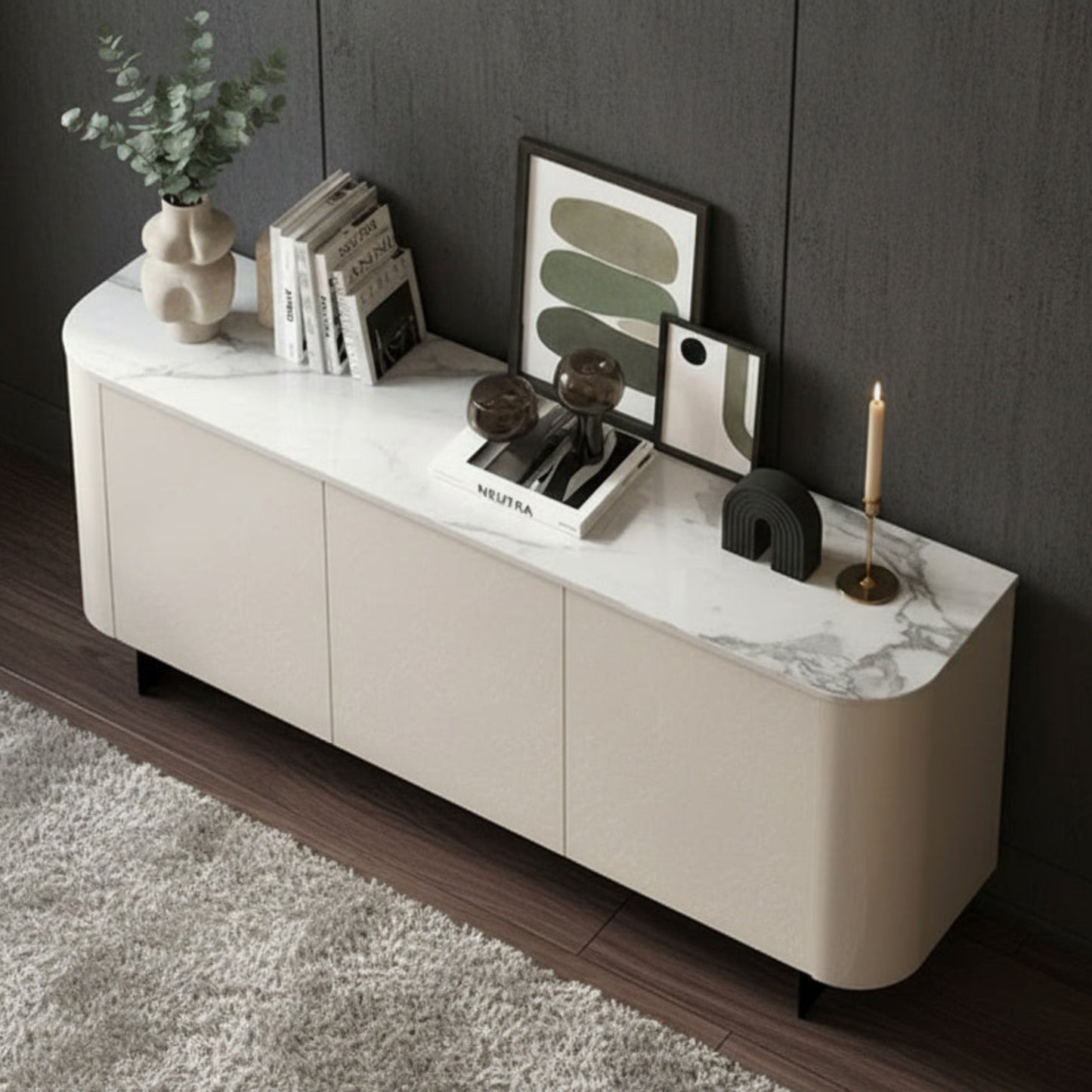 A modern cream-colored media console with a white and gray marble top, styled with books, a plant, and framed art in a dark room.