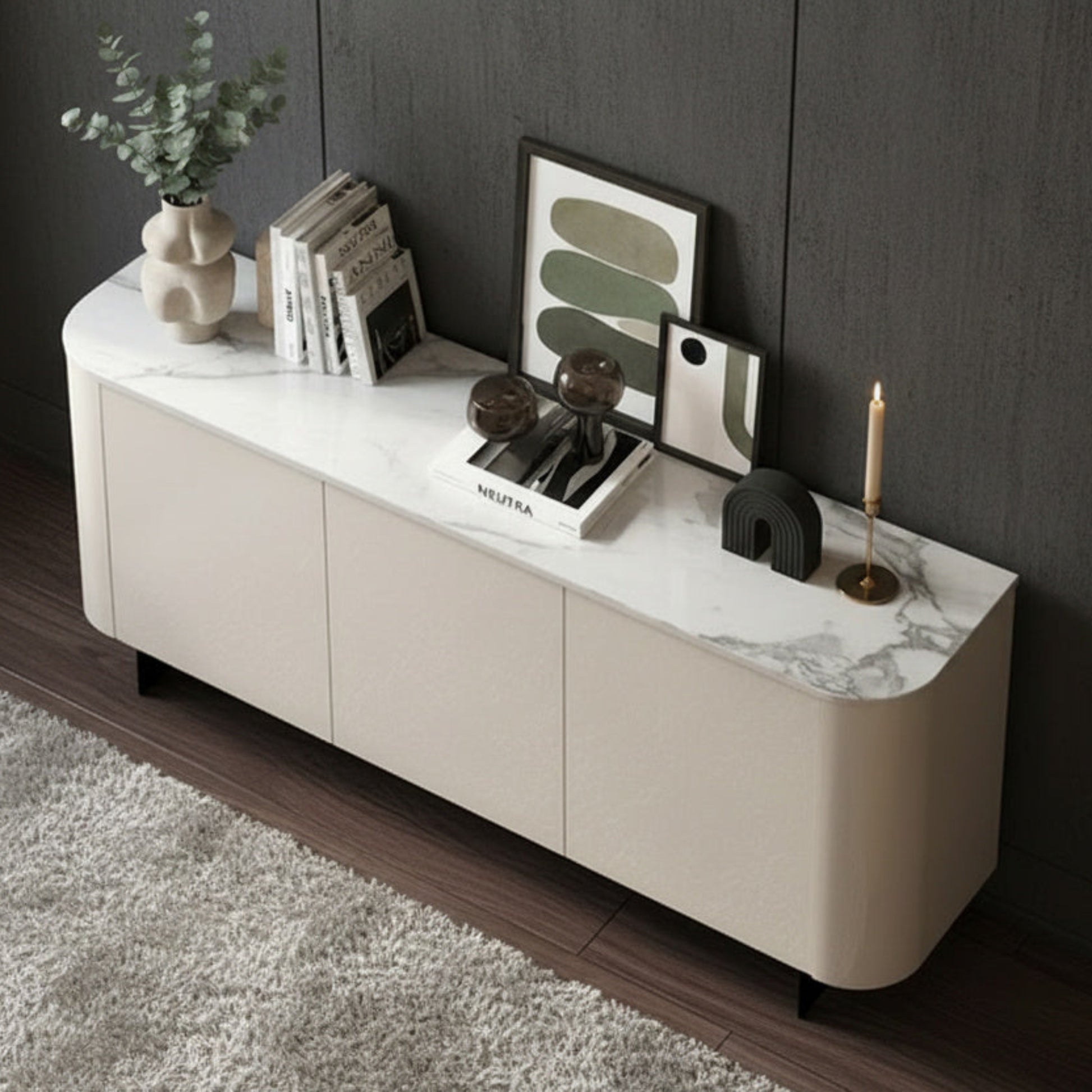A modern cream-colored media console with a white and gray marble top, styled with books, a plant, and framed art in a dark room.