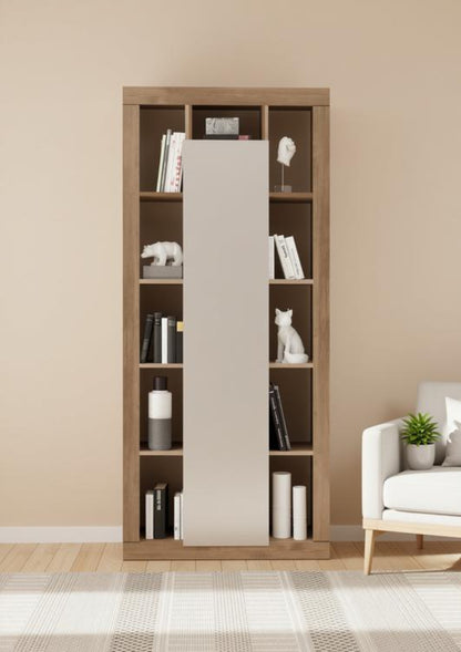 A tall wooden bookcase with sliding doors in a warm medium brown finish, styled with books, white decorative figurines, and cylindrical vases, set against a beige wall in a modern living room next to a white armchair.