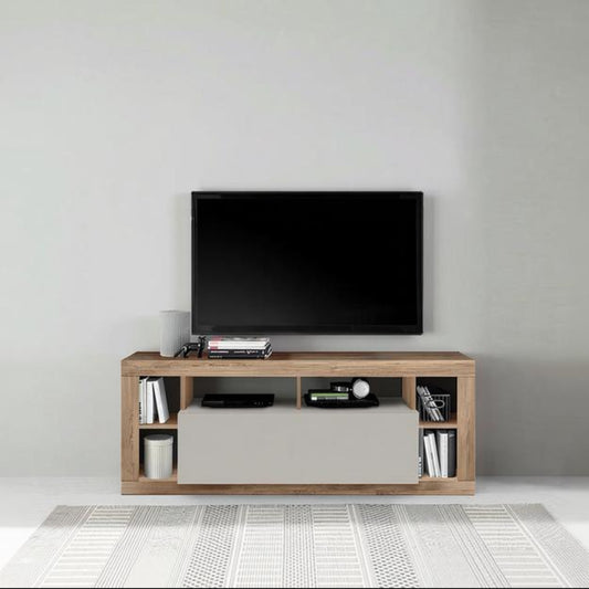 A modern wooden TV stand console with a light oak finish and a central cream drawer, styled with a black flat-screen TV, electronic devices, and books, set against a minimalist gray wall and white patterned rug.